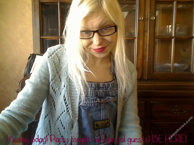 Sunny Crittenden on her birthday in 2015. She has long bleach blonde hair, black glasses, and bright magenta lipstick. She is wearing denim overalls and a light blue knitted cardigan.