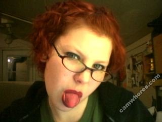 A 320x240 pixel webcam photo of Sunny Crittenden circa 2007. She has short, curly red hair and black glasses, and she is sticking out her tongue. The photo has a Camwhores.com watermark on it.
