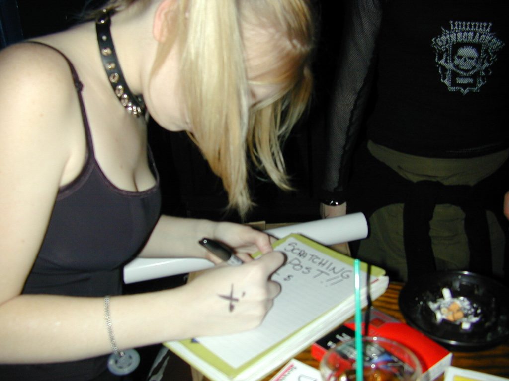 A photo of Sunny Crittenden writing out prices at the Scratching Post merch booth.