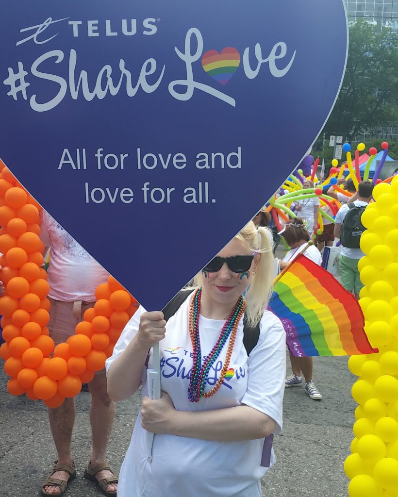 A photo of Sunny holding a purple, heart-shaped "#ShareLove" protest sign during Toronto's Pride Parade in 2016.