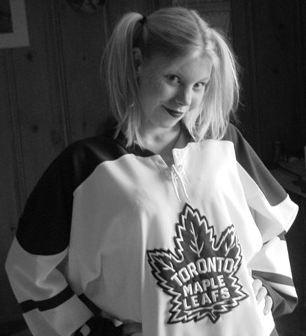 A black and white photo of Sunny Crittenden circa 2001, when she was 22. She is wearing a vintage inspired Toronto Maple Leafs jersey and has her long blonde hair in pigtails.